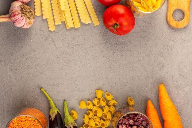 Uma vista superior macarrão cru amarelo seco italiano longo macarrão, juntamente com tomates vermelhos, berinjelas, cenouras e alho, isolado no fundo cinza legumes comida refeição