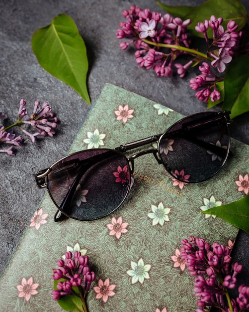 Uma vista superior óculos de sol pretos modernos sobre o fundo cinza, juntamente com flores roxas e folhas isoladas elegância de óculos de visão