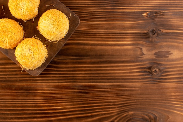 Uma vista superior redonda bolos doces deliciosos bolos saborosos isolados alinhados na mesa rústica de madeira marrom e fundo marrom biscoito doce de açúcar