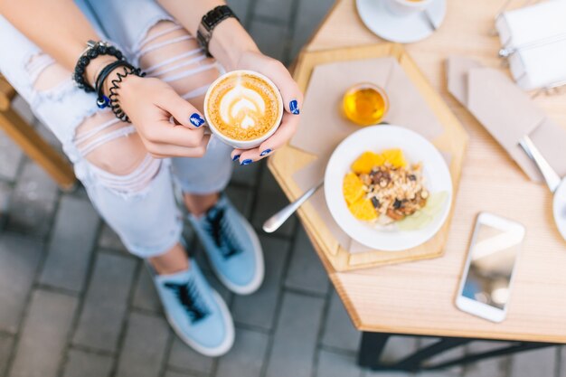 Uma xícara de café com desenho nas mãos de uma jovem sentada no terraço