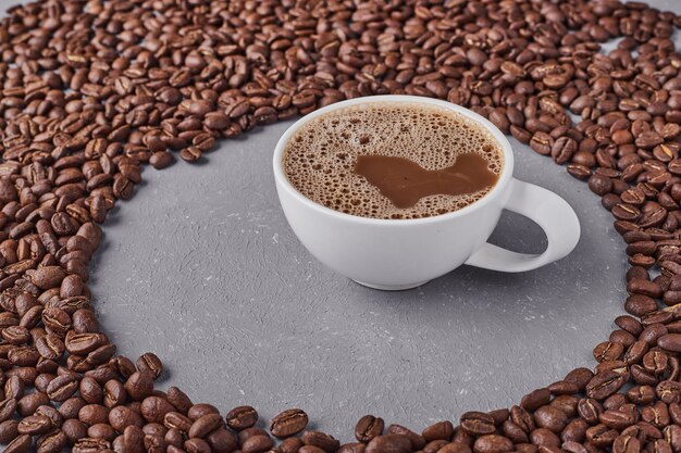 Uma xícara de café com grãos de arábica ao redor.