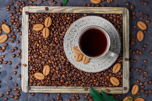 Uma xícara de café com grãos de café torrados e grãos de café em forma de biscoitos na superfície escura