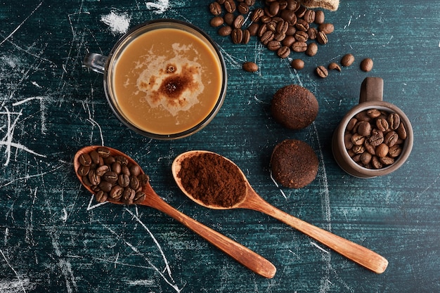 Uma xícara de café com grãos e biscoitos ao redor.