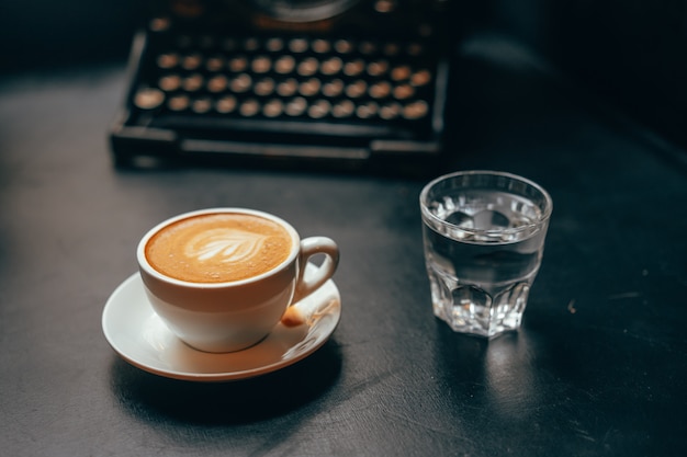 Uma xícara de café com leite em uma xícara de cerâmica e um copo de água