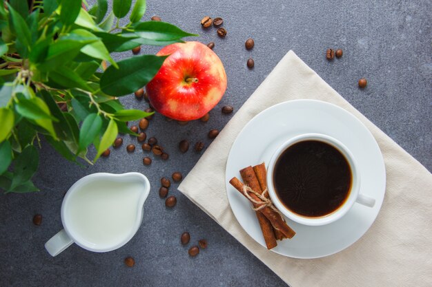 Uma xícara de café com maçã, canela seca, planta, vista superior de leite sobre uma superfície cinza