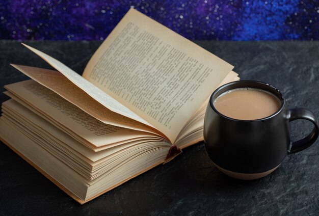 Uma xícara de café com um livro sobre uma superfície escura.