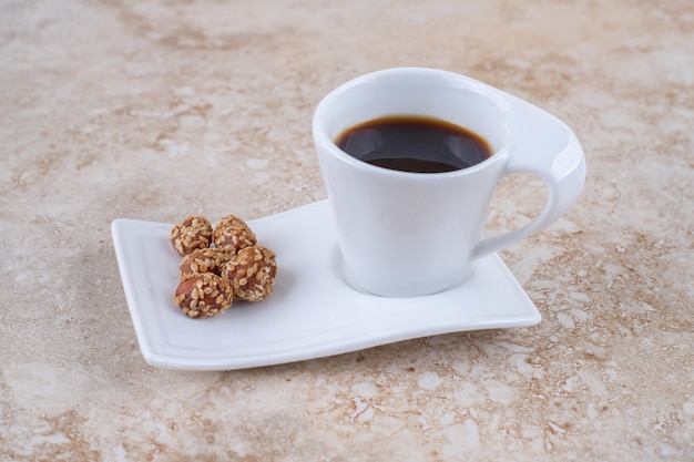 Uma xícara de café e amendoim glaceado em uma travessa