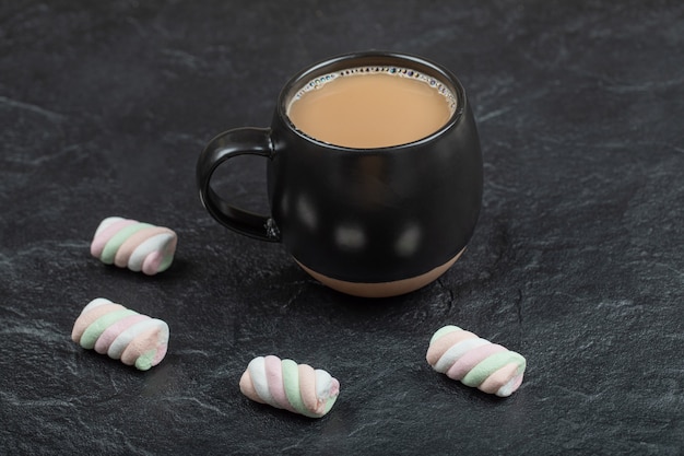 Uma xícara de café preta com marshmallows em uma superfície escura.