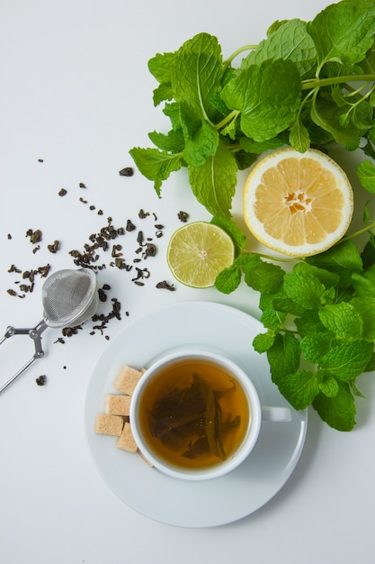 Uma xícara de chá com limão, açúcar, folhas de hortelã vista superior em uma superfície branca