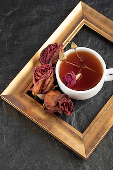 Uma xícara de chá com rosa seca e moldura em uma mesa preta.