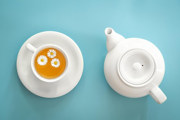 Uma xícara de chá de camomila e um bule em um fundo azul
