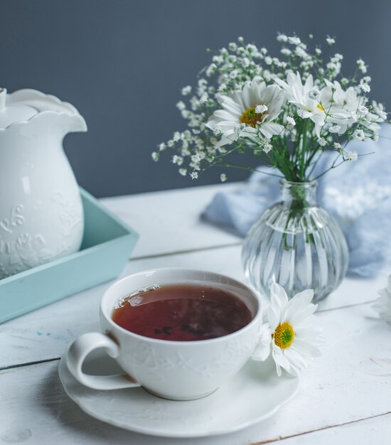 Uma xícara de chá e margaridas brancas em uma mesa branca.