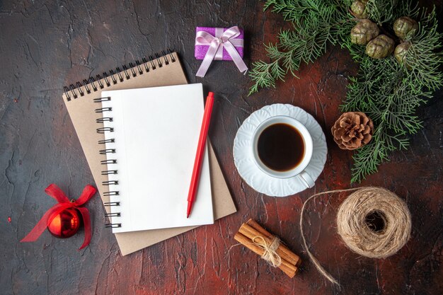Uma xícara de chá preto, acessórios de decoração de ramos de abeto e um presente ao lado de um caderno com uma caneta em fundo escuro