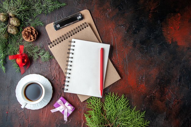 Uma xícara de chá preto, acessórios de decoração de ramos de abeto e um presente ao lado do caderno com fundo escuro de penon