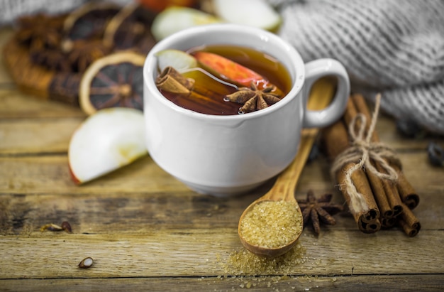 uma xícara de chá quente com um pau de canela e uma colher de açúcar mascavo na madeira