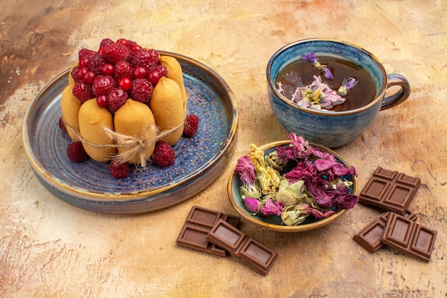 Foto grátis uma xícara de chá quente de ervas bolo macio com frutas flores e barras de chocolate na mesa de cores misturadas