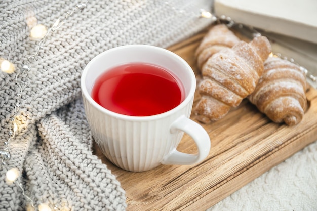 Uma xícara de chá vermelho, um croissant e um elemento de malha em uma bandeja de madeira