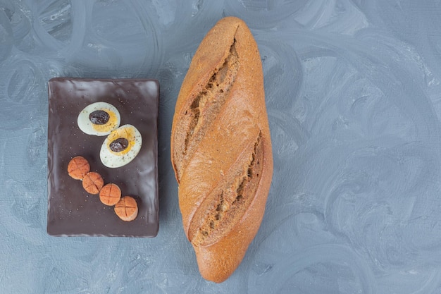 Única carga de pão ao lado do prato de linguiça e fatias de ovo na mesa de mármore.