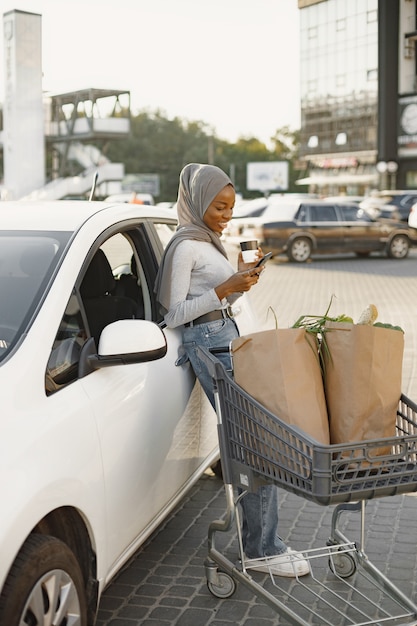 Usando o smartphone enquanto espera. mulher de etnia africana na estação de carga de carros elétricos durante o dia. veículo totalmente novo.