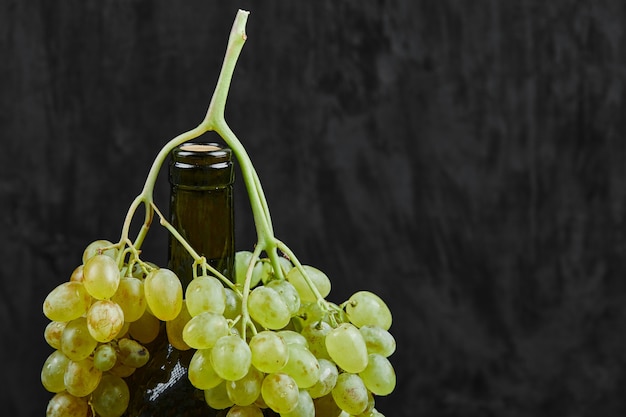 Foto grátis uvas brancas e uma garrafa de vinho na superfície escura