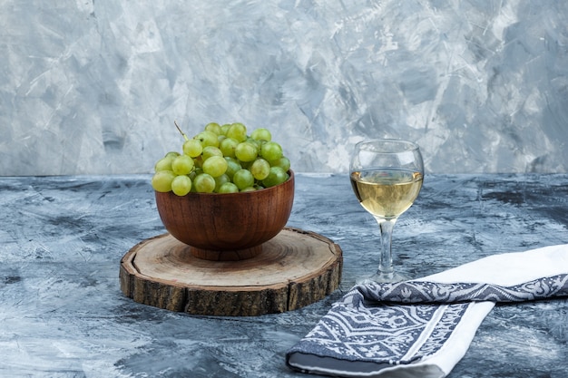 Uvas brancas, nozes em uma tábua de cortar com um copo de uísque, close-up de toalha de cozinha em um fundo de mármore azul claro e escuro