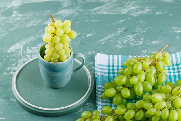 Foto grátis uvas com bandeja em um copo de gesso e fundo de pano de piquenique, vista de alto ângulo.