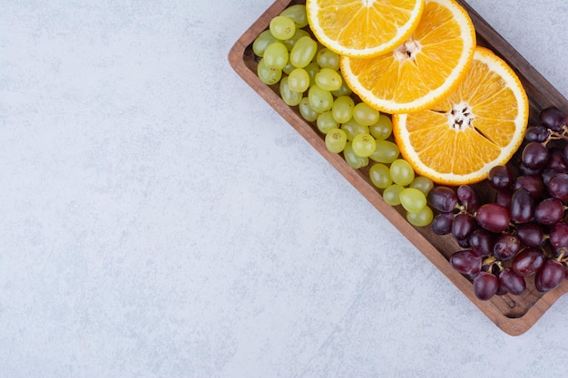 Uvas e fatias de laranja na placa de madeira.