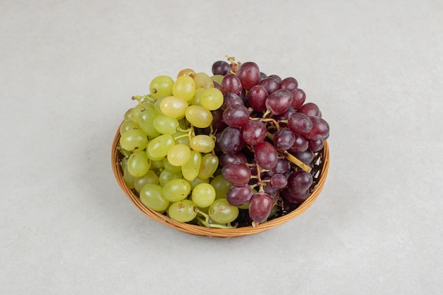 Uvas frescas de vermelhas e verdes em uma cesta de madeira.