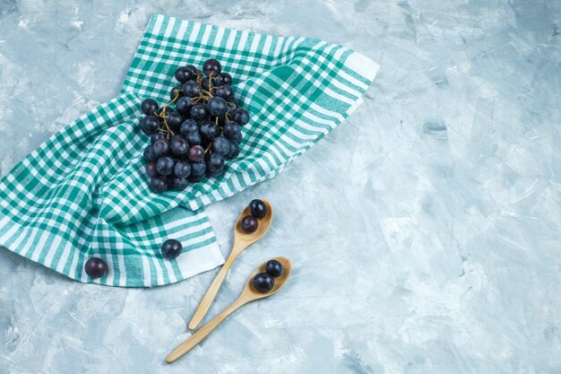 Foto grátis uvas pretas em colheres de madeira em fundo cinza sujo e toalha de cozinha. colocação plana.