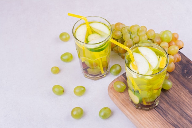 Uvas verdes com dois copos de suco em uma placa de madeira