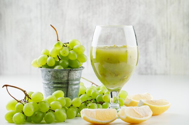 Uvas verdes com rodelas de limão, coquetel de uva em um mini balde na superfície branca