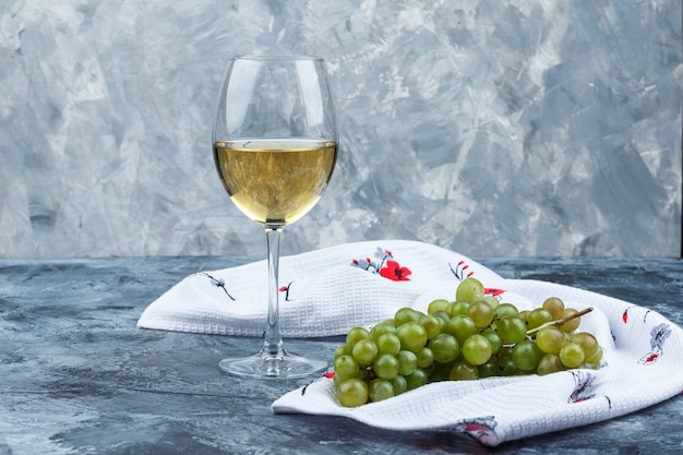 Foto grátis uvas verdes com um copo de vinho no fundo de gesso e toalha de cozinha sujo, vista lateral.