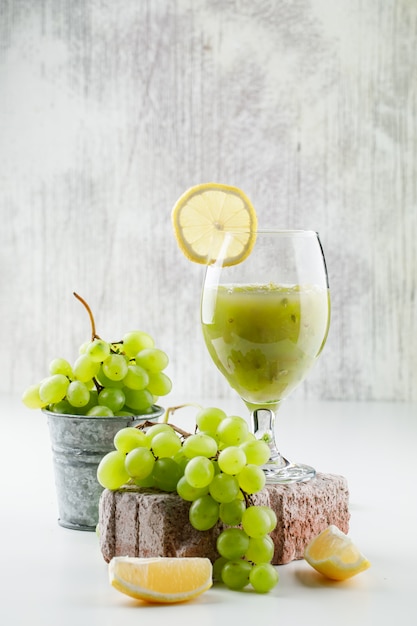 Uvas verdes em um mini balde com fatias de limão, tijolo, coquetel de uva vista lateral na parede branca e suja