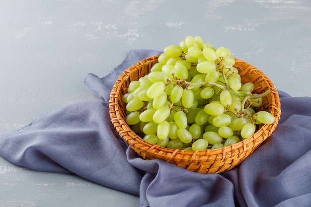 Uvas verdes em uma cesta de vime em têxteis e gesso, vista de alto ângulo.