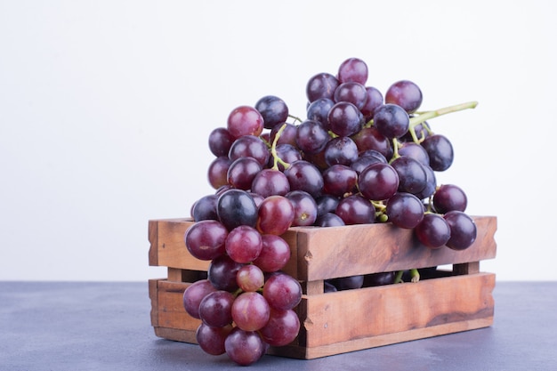 Uvas vermelhas em uma bandeja de madeira na superfície azul