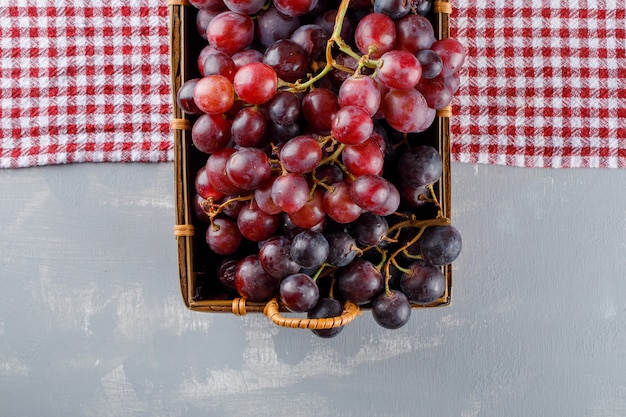 Foto grátis uvas vermelhas em uma cesta plana sobre uma toalha de piquenique e gesso