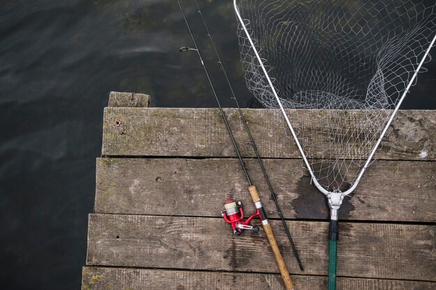 Vara de pesca e rede de pesca na beira do cais de madeira sobre o lago