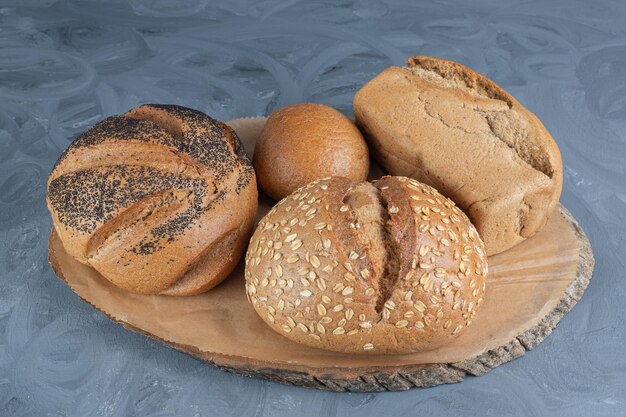 Variedade de pães em uma placa de madeira na mesa de mármore.