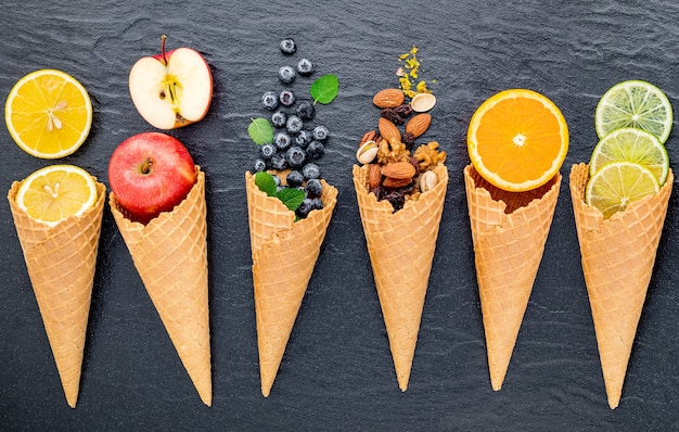 Vários ingredientes para sabor de sorvete em cones configurados em fundo de pedra escura.