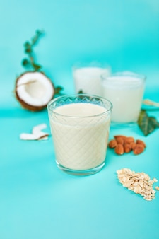 Vários leites e ingredientes vegetais veganos, leite não lácteo, tipos alternativos de leites veganos em copos sobre um fundo azul com espaço de cópia