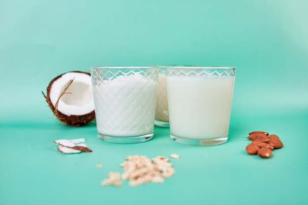 Vários leites e ingredientes vegetais veganos, leite não lácteo, tipos alternativos de leites veganos em copos sobre um fundo azul com espaço de cópia