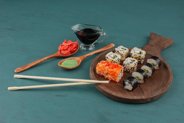 Vários tipos de prato de rolo de sushi com gengibre em conserva, wasabi e molho de soja na mesa azul.