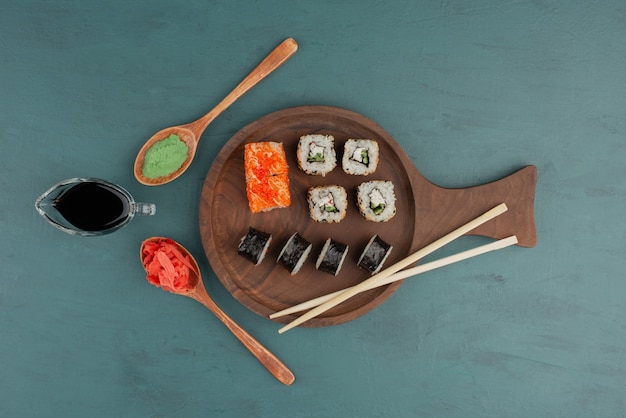 Vários tipos de prato de rolo de sushi com gengibre em conserva, wasabi e molho de soja na mesa azul.