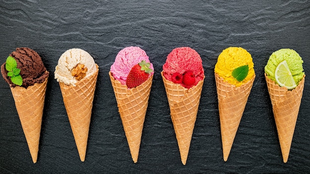 Vários tipos de sabor de sorvete em cones configurados em fundo de pedra escura.