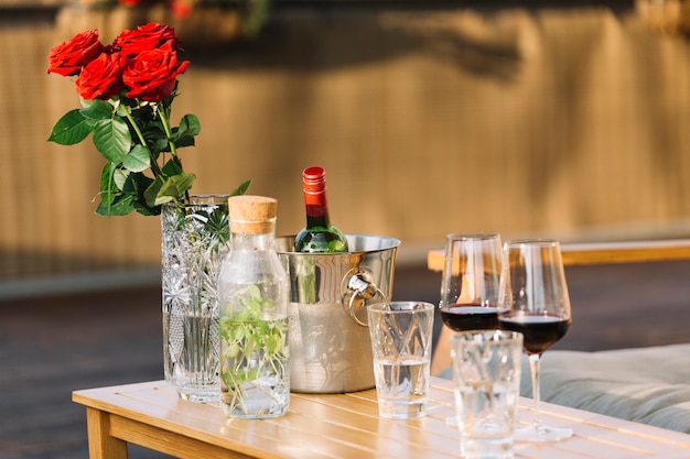 Vaso de rosas vermelhas; balde de gelo e taças de vinho na mesa de madeira