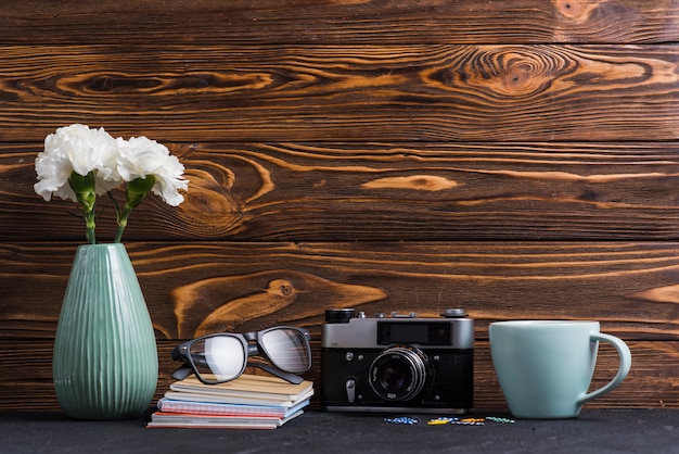 Vaso; livros; Óculos; clipe de papel; Copa e câmera retro na mesa preta contra o fundo de madeira