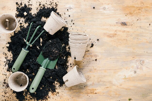 Vasos de turfa e ferramentas de jardinagem com solo preto liso na mesa de madeira