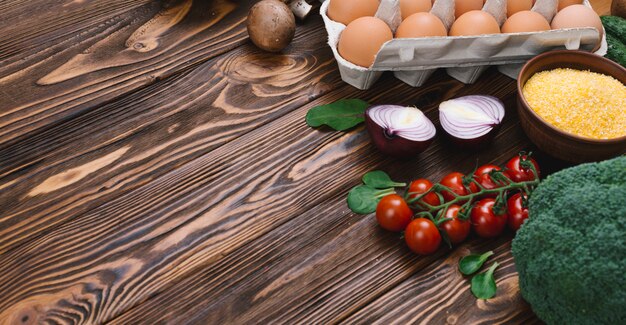 Vegetais frescos; ovos e tigela de polenta sobre a mesa de madeira