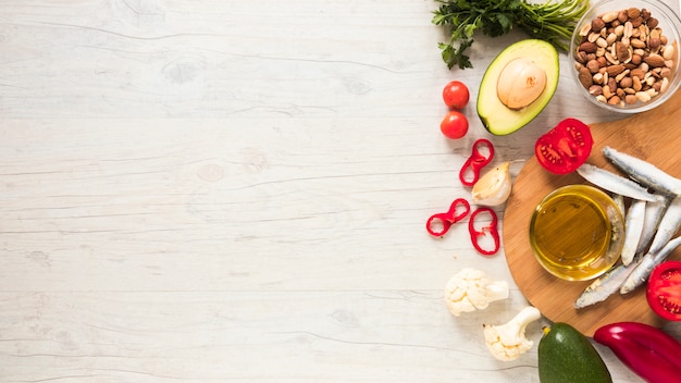 Vegetais saudáveis; frutas secas; óleo e peixe cru na mesa de madeira