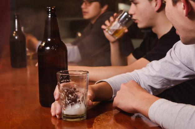 Veja o detalhe de um jovem segurando um copo enquanto seus amigos bebem cerveja, no bar.